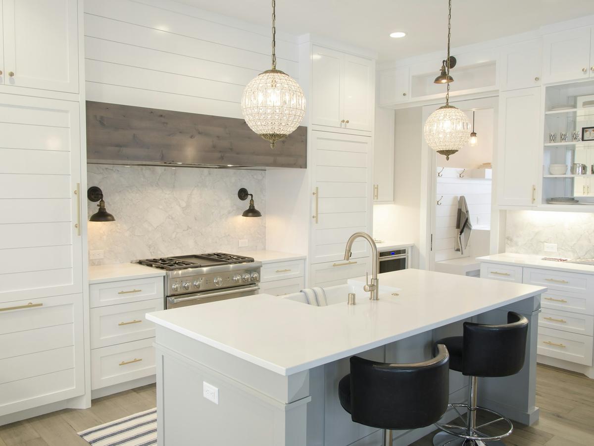 A bright white kitchen with a clean island, shining counters, and pendant lights.
